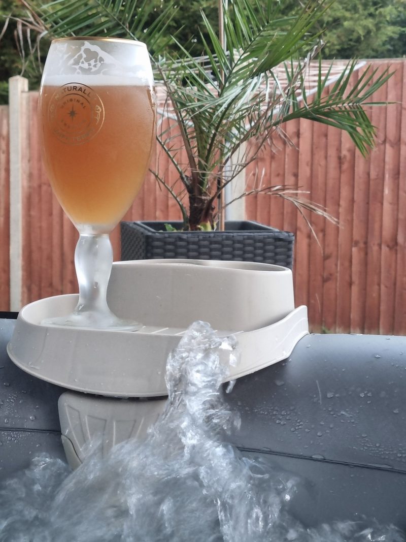 A cold drink resting on the edge of a hot tub in a garden