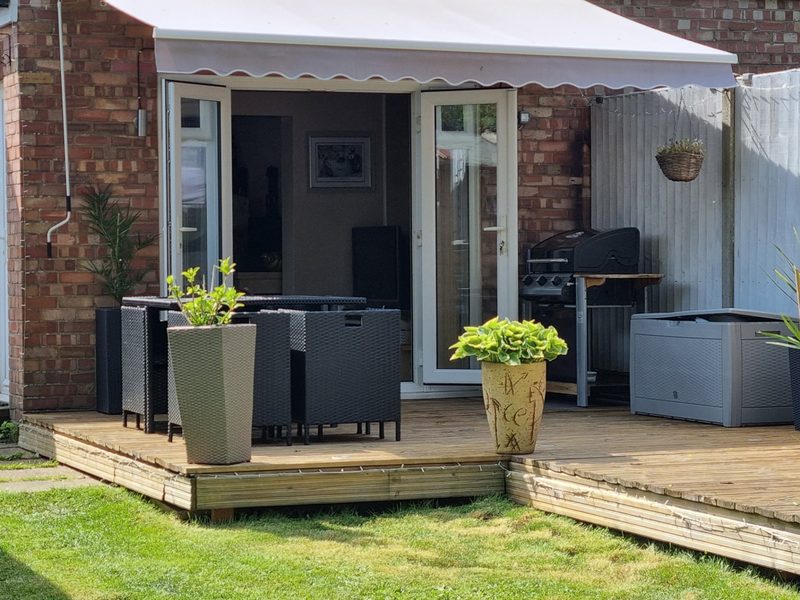 The finished deck with rattan furniture, an awning, a barbecue and a storage box
