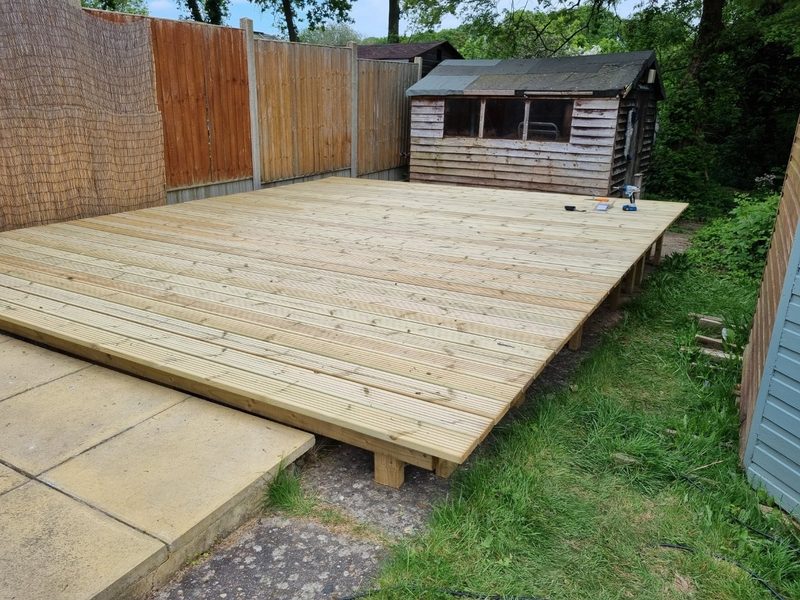 A newly built timber deck in a back garden, with a shed behind it