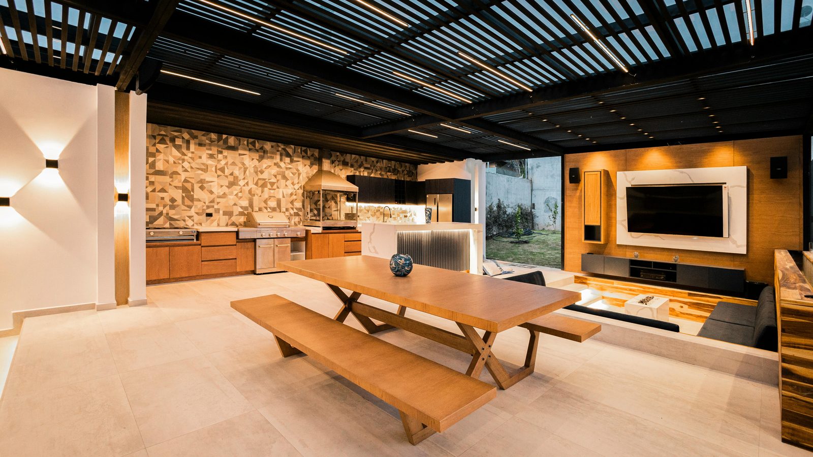 A modern covered outdoor room with a long table and a screen